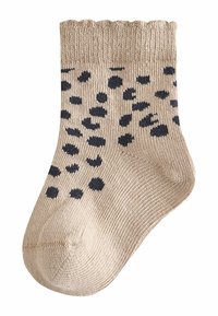 Beige knitted sock with a ribbed cuff, featuring black circular dots throughout the body and a smooth texture.