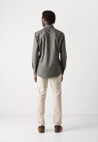 Graues Button-Down-Hemd mit langen Ärmeln, taillierter Schnitt, glattes Material und Schulterpasse, kombiniert mit hellbeigen Hosen und dunklen Schuhen.