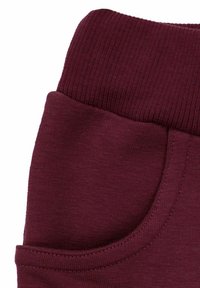 Bordowe bawełniane dresy z prążkowanym pasem i boczną kieszenią, o gładkiej fakturze i obszytych krawędziach.