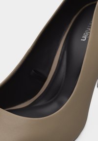 Gros plan sur une chaussure à talon beige avec une semelle intérieure noire et une finition mate lisse.