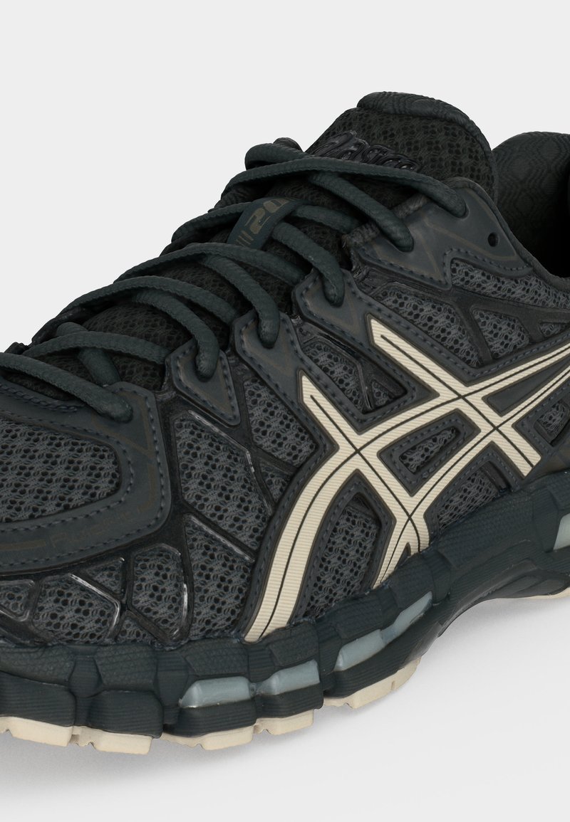 Zapatilla de running de malla negra y material sintético con logo blanco de Asics, cordones negros y suela segmentada con detalles en gris claro y beige.