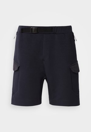 Mørkeblå shortser laget av et glatt stoff med belte, med to sidelommer og vinklede detaljer på beina.