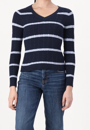 Marineblauwe kabelgebreide V-hals trui met lichtblauwe horizontale strepen, gedragen met medium blauwe spijkerbroek.