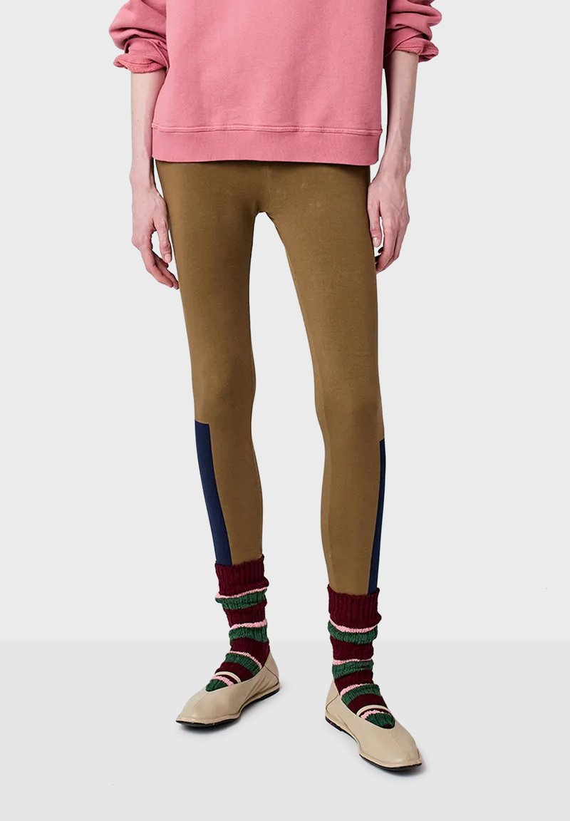 Brown stretchy leggings with dark blue side panels, paired with red and green striped socks and beige slip-on shoes; worn under a pink sweatshirt.