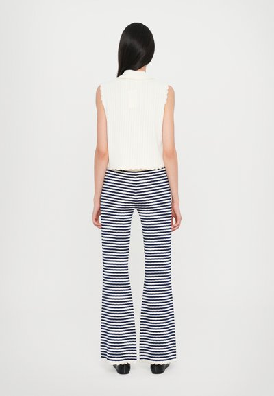 Gilet en maille cropped ivoire avec un motif texturé et un col festonné, associé à un pantalon évasé rayé bleu marine et blanc.