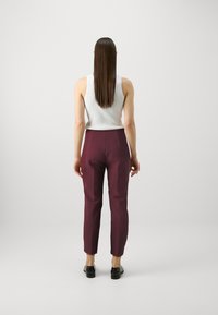 Burgundske krojene hlače s uskim siluetom, glatkom teksturom i srednjim strukom, u kombinaciji s bijelim tank topom s rebrastim uzorkom.