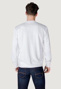 Felpa bianca con collo a giro e maniche lunghe, polsini a costine e un tessuto morbido e texturizzato. La vista posteriore mostra linee pulite e nessuna grafica.