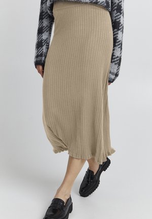 Beige gerippter Midirock mit ausgestellt geschnittenem Saum und strukturiertem Stoff. Getragen mit einem gemusterten Pullover und schwarzen Loafers.