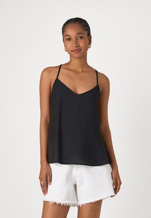 Camisole en satin noir avec un décolleté en V et des bretelles fines, présentant une coupe décontractée et une texture lisse. Porté avec des shorts blancs effilochés.