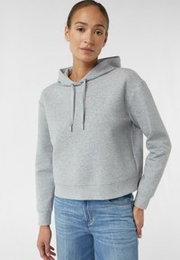 Grau geschnittenes Hoodie mit Kordelzugkapuze, mit kleinem Logo auf der Brust und gerippten Bündchen, kombiniert mit blauen Jeans.