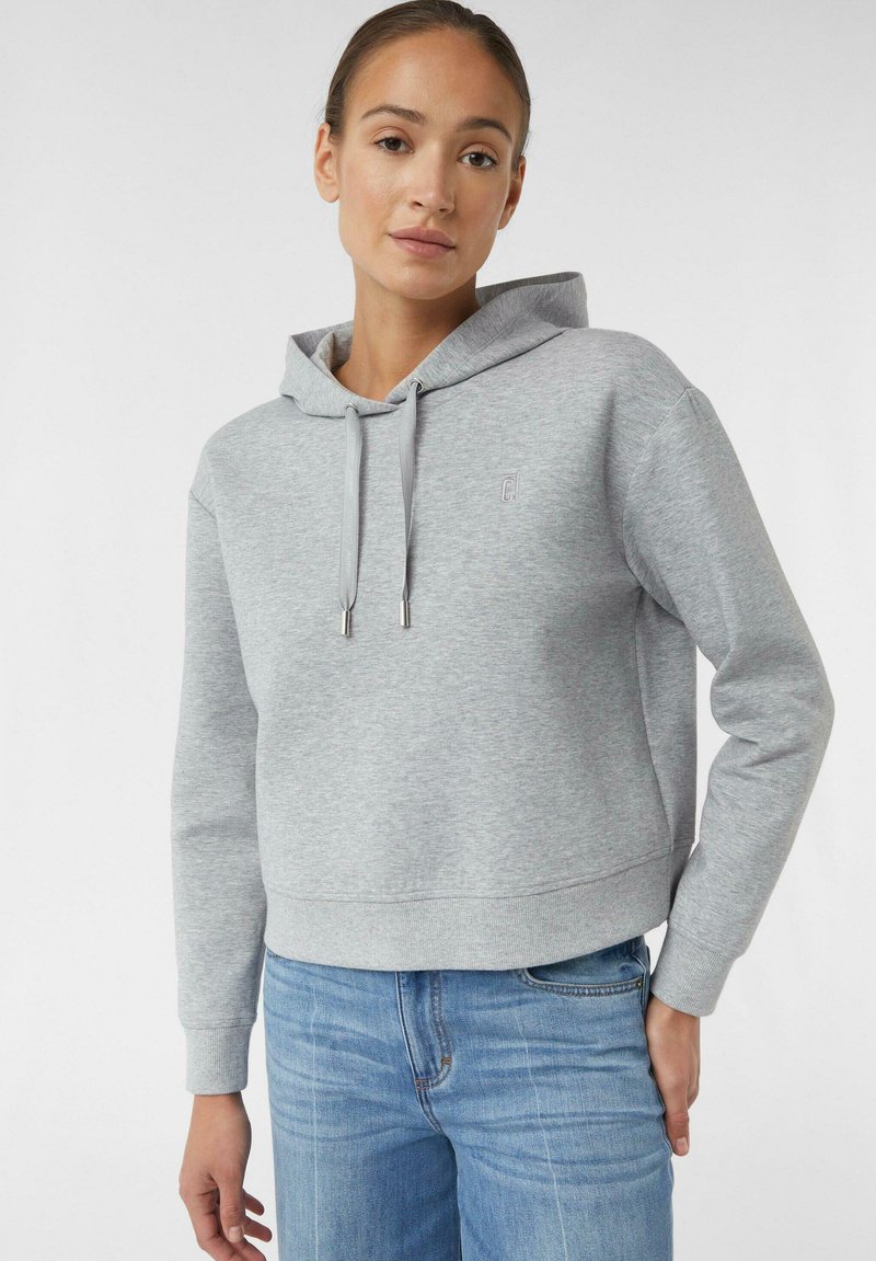 Grau geschnittenes Hoodie mit Kordelzugkapuze, mit kleinem Logo auf der Brust und gerippten Bündchen, kombiniert mit blauen Jeans.