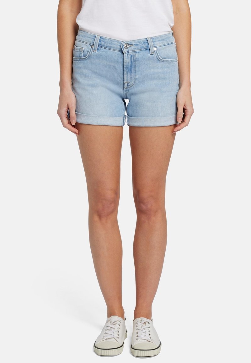 Shorts in denim azzurro chiaro con orlo risvoltato, cinque tasche e design aderente, abbinati a sneakers bianche.