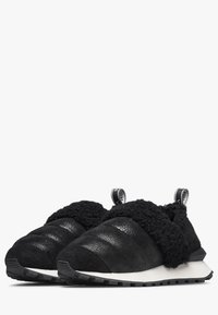 Scarpe slip-on nere con tomaia testurizzata e finitura scamosciata, colletto morbido e suola bianca a contrasto con un motivo di battistrada robusto.