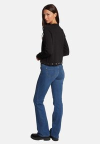 Chaqueta negra corta con acentos de anillo en el dobladillo, combinada con jeans acampanados azules. Textura suave, diseño sencillo y silueta ajustada.