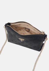 Schwarze Guess Leder-Umhängetasche mit eingeprägtem Logo-Muster, goldfarbener Kettenriemen und beigem Stofffutter mit Reißverschlusstasche.