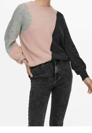 Femme portant un pull color block avec des sections roses, grises et noires, associé à un jean noir délavé taille haute.