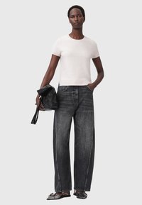 Maglione aderente grigio chiaro a maniche corte abbinato a jeans neri in denim larghi. Il modello tiene una borsa in pelle nera, le scarpe sono scure e flat.