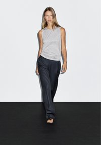 Grå ärmlös topp och lösa svarta byxor. Toppen har en rund halsringning, medan byxorna har en avslappnad passform och slät textur.