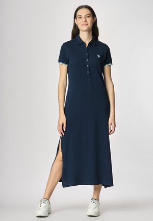 Abito polo navy con maniche corte, pattina dei bottoni, spacco laterale e accenti a strisce contrastanti. Indossato con sneakers bianche.