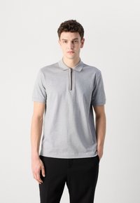 Šedé polo tričko so zipsom, krátkymi rukávmi a klasickým golierom. Mäkka textúra a prispôsobený strih, v kombinácii s čiernymi nohavicami.