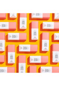 Pink and white eye cream bottles arranged on a bright orange background. Bottles feature a pump top and labels with product information.