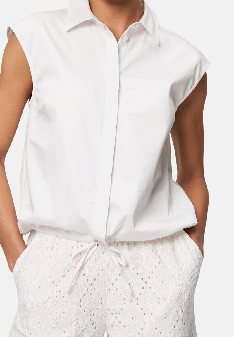 Chemise blanche à manches courtes avec col, en tissu léger, associée à un short blanc texturé avec un motif et une taille à cordon.