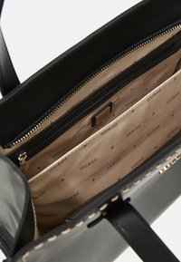 Schwarze Handtasche mit glatter Außenseite, Reißverschluss und beiger Innenausstattung mit wiederholtem Logo-Muster. Enthält Innenfächer und Kartensteckplatz.