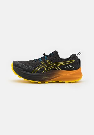 Chaussure de trail running noire et jaune avec semelle texturée, lacets bleus et languette au talon sur fond blanc.