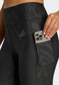 Schwarze Sportleggings mit einem subtilen strukturierten Design, ausgestattet mit einer Seitentasche für ein Smartphone und einem adidas-Logo auf dem Bund.