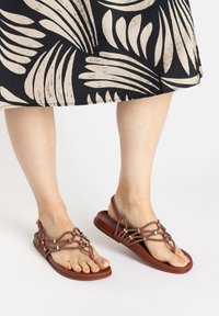 Braune Riemchensandalen mit flacher Sohle und geflochtenen Schnurdetails. Das Design verfügt über einen Zehenring und verstellbare Riemen für einen sicheren Sitz.