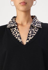 Maglietta nera a V con colletto in stampa leopardata, dotata di una texture liscia e un netto contrasto di colore tra la parte nera e i motivi beige.
