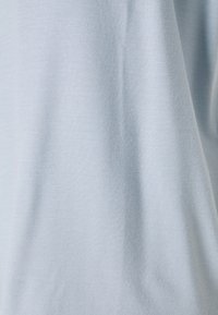 Tissu en coton bleu clair avec une surface lisse, légèrement texturée et des plis souples et fluides.