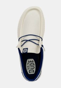 Scarpa slip-on bianca in tela con un accento blu intorno al colletto, dotata di un sottile lacci e un interno imbottito. Logo visibile sulla linguetta.