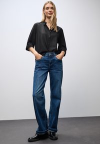 Czarna bluzka na guziki z podwiniętymi rękawami, zestawiona z niebieskimi, wysokimi dżinsami. Dżinsy mają luźny krój i widoczne detale przeszycia.