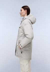 Parka de color gris claro acolchada con capucha, dos bolsillos frontales y botones negros. Tejido texturizado con un acabado mate, diseño casual.