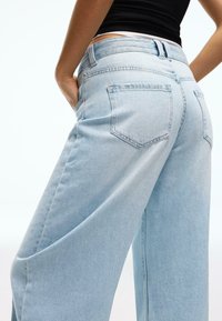 Blugi din denim albastru deschis cu croială largă, talie înaltă, buzunare în partea din spate și detalii subtile de cusături. Textură netedă, croială casual.