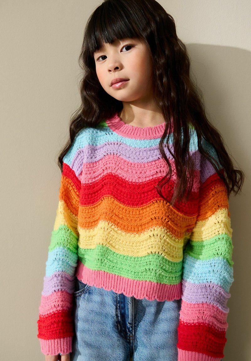 Pull tricoté présentant des rayures ondulées aux couleurs de l'arc-en-ciel : rouge, orange, jaune, vert, bleu et violet. Design court avec bords côtelés.