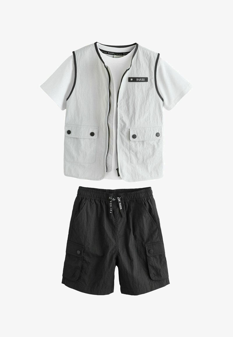 Balti trumpomis rankovėmis marškiniai su šviesiai pilka berankove liemene, kurioje yra priekinės kišenės, derinami su juodais kargo šortais, turinčiais kišenes su sagomis ir raišteliu juosmens srityje.