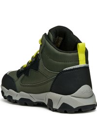 Chaussure de randonnée mi-haute en tissu vert foncé avec des accents noirs. Avec une semelle en caoutchouc grise, des lacets jaunes et un renfort au talon pour un soutien.