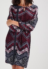 Rotes und marineblau gemustertes Kleid mit langen Ärmeln, das über einen Schlüsselloch-Ausschnitt, ein Zickzackdesign und detaillierte Blumenakzente verfügt. Weicher Stoff.