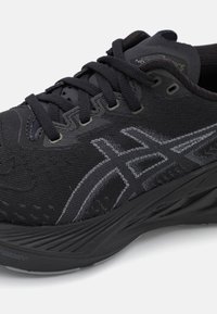 Chaussure de sport noire avec une tige en tricot, présentant des motifs texturés et des accents réfléchissants. Semelle extérieure en caoutchouc avec un relief prononcé.