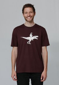 Bordeaux-kleurige katoenen T-shirt met een witte afbeelding van een astronaut die op een dinosaurus rijdt, korte mouwen, ronde hals en een ontspannen pasvorm.