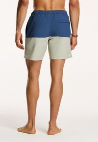 Heren zwemshorts met een elastische tailleband. Donkerblauw bovenstuk en lichtgroen onderstuk, met een achterzak en een gladde textuur.