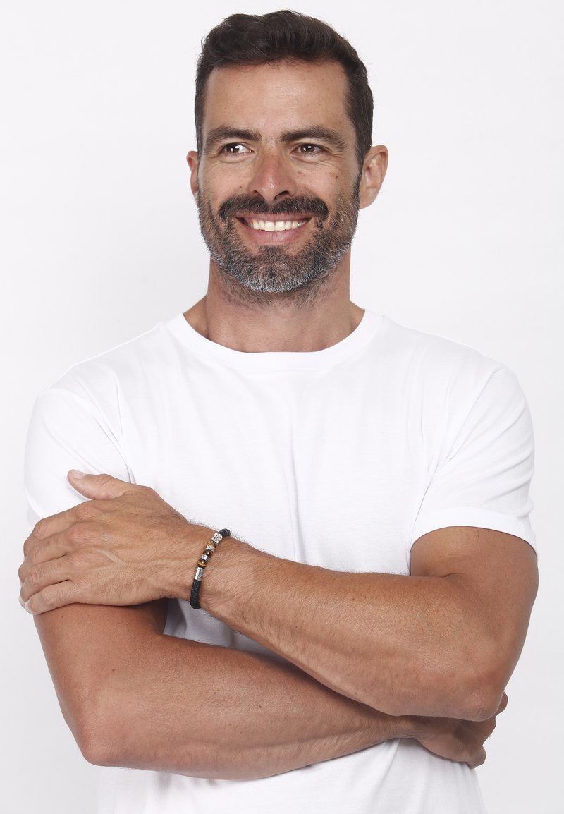 Black leather bracelet with metallic beads, worn on a tanned arm, paired with a white t-shirt, showcasing a casual design and texture.