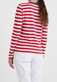 Maglietta a maniche lunghe con righe orizzontali rosse e bianche, in morbido cotone, collo a giro e vestibilità comoda. Pantaloni bianchi visibili.