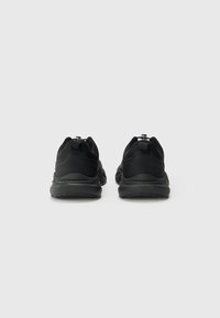 Baskets de sport noires avec une tige en mesh texturé, un col rembourré et une semelle amortissante. Dispose d'une languette au talon pour une mise enfile facile.