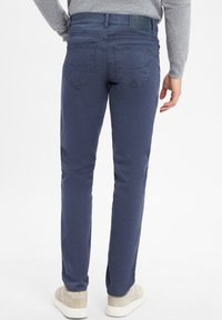 Pantalons slim-fit bleu marine en tissu mélangé coton, avec poches arrières et étiquette texturée à la taille. Portés avec des baskets décontractées.