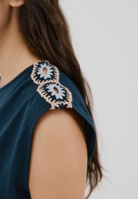 Dunkelblau-grünes Oberteil mit kurzen Ärmeln, das auf der Schulter mit aufwendigen gestickten Blumenmotiven in Blau und Beige verziert ist. Glatte Textur.