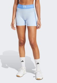 Pantaloni shorts atletici di colore azzurro chiaro con vita alta, caratterizzati da strisce laterali e una texture liscia e elastica. Indossati con calze bianche e scarpe.