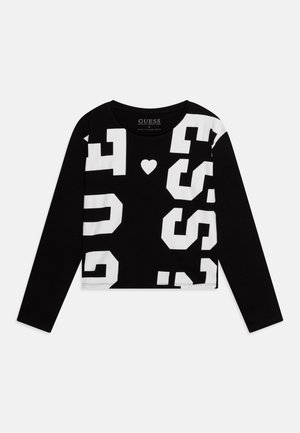 Sort crop top med lange ærmer, store hvide "GUESS"-bogstaver og et lille hvidt hjerte midt på fronten.